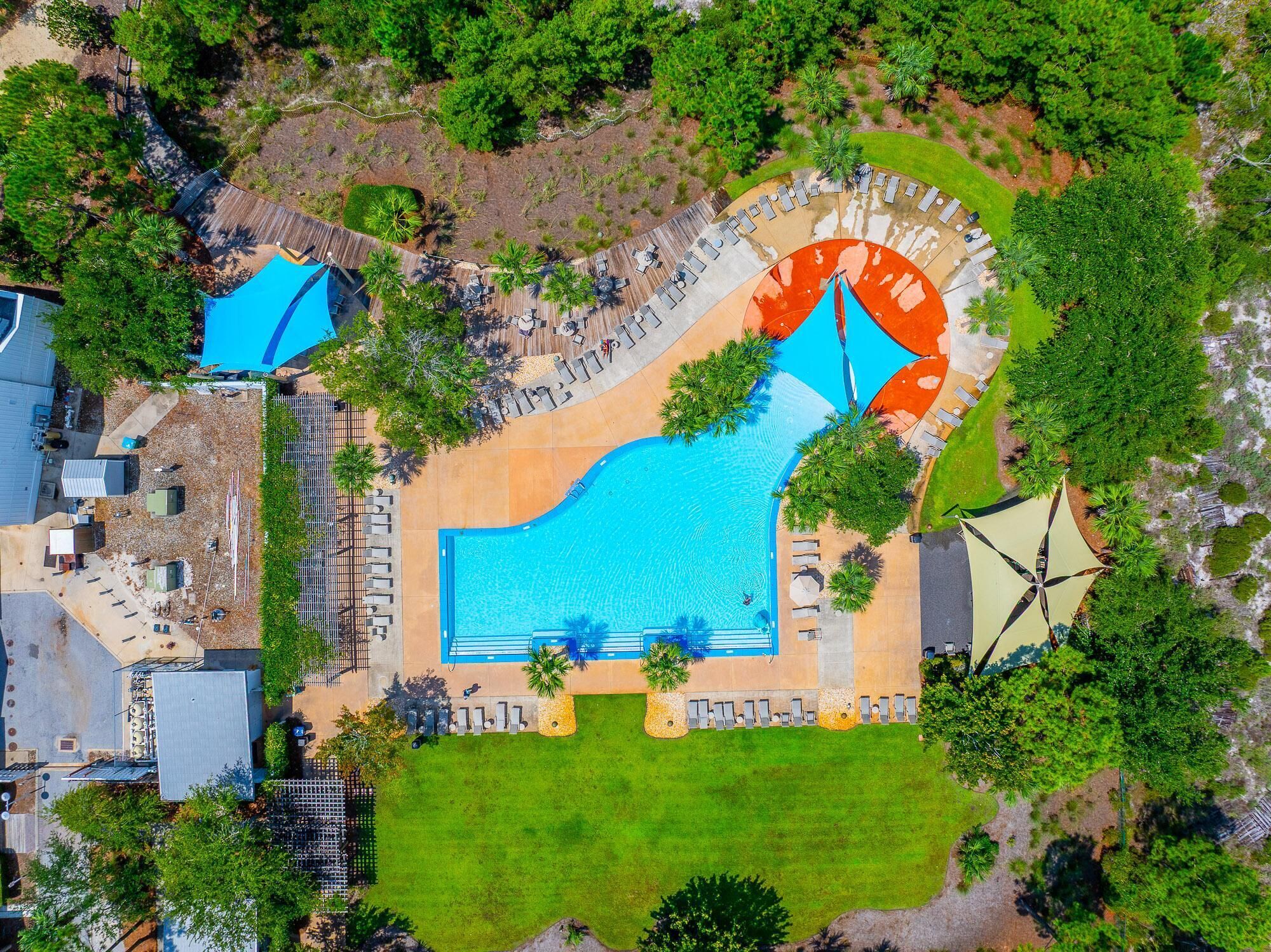 Vue aérienne d’un complexe hôtelier doté d’une grande piscine, de chaises longues et d’un espace abrité.