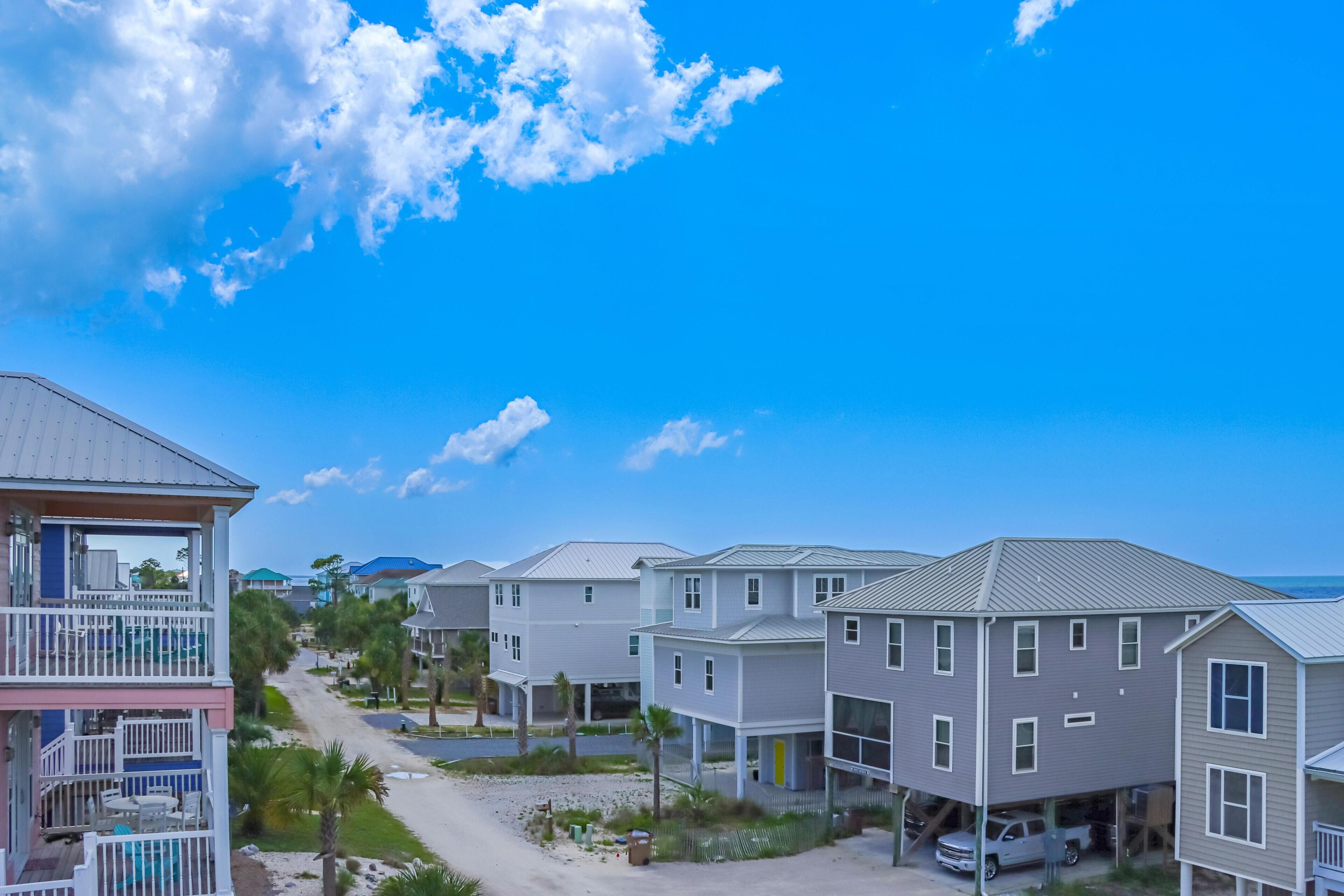 A coastal residential area with multi-story houses, a clear sky, and a sandy path leading to the beach.