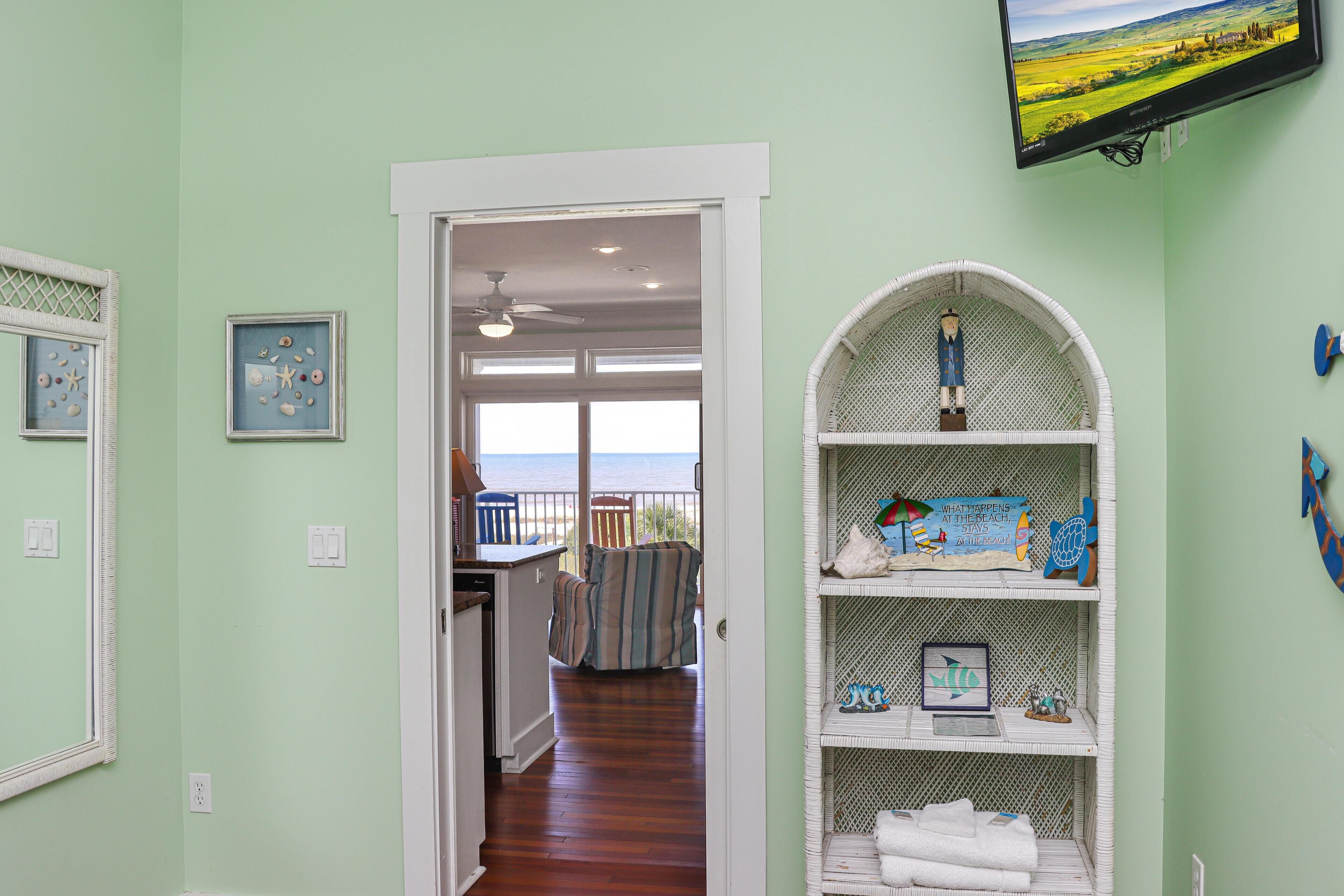 A room with a view of the ocean, a white arched shelving unit with various items, and a door leading to another room.