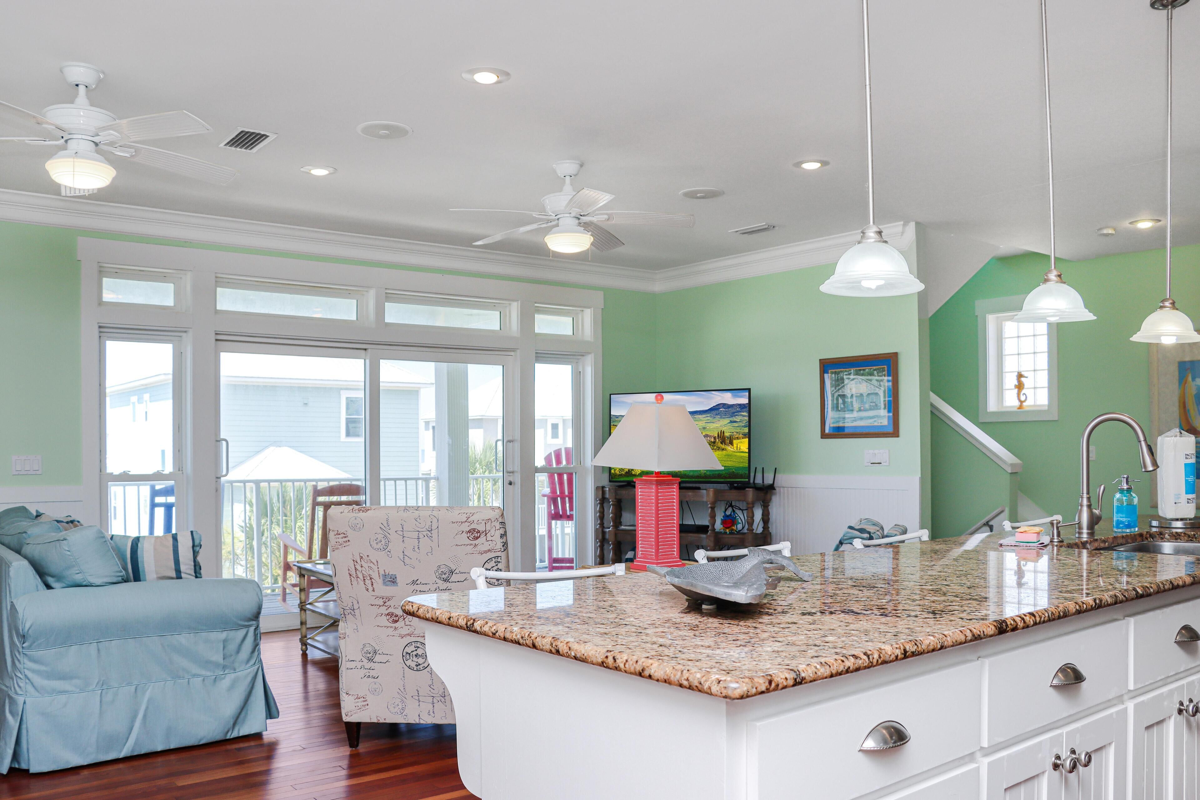 A modern kitchen with a granite countertop, white cabinetry, and a ceiling fan.