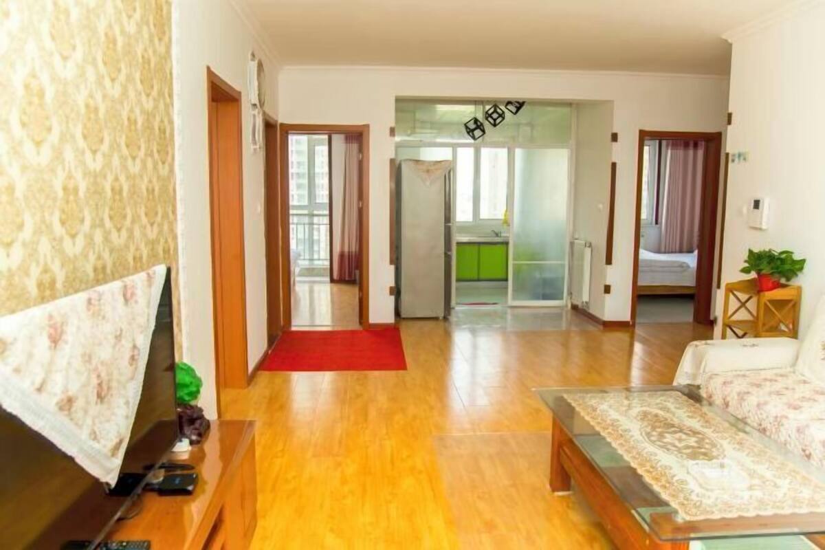 A modern living room with a wooden floor, a sofa, a TV, and a red rug.