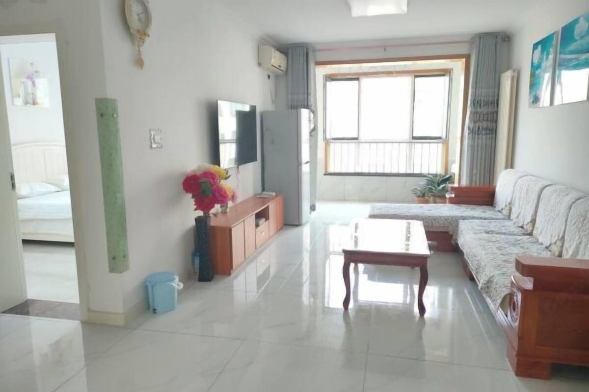 A living room with a sofa, a coffee table, a TV, and a window with curtains.