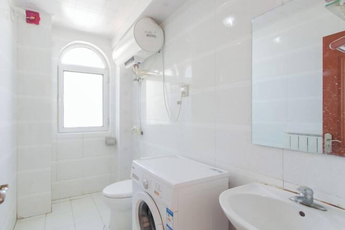 A bathroom with a washing machine, a sink, and a window.