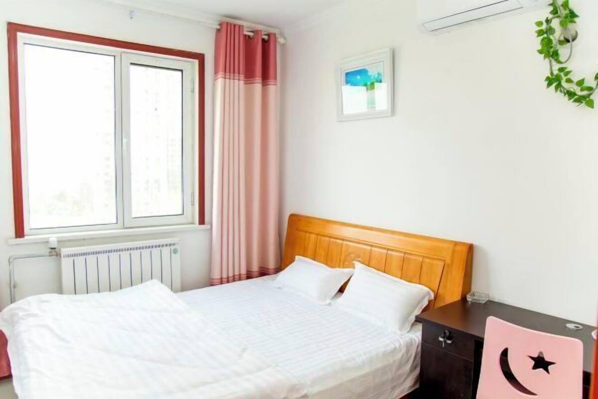A bedroom with a bed, a nightstand, a dresser, a window with curtains, a radiator, and a wall-mounted picture.