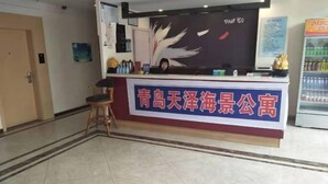 Un mostrador de recepción con un cartel en caracteres chinos, una silla, una pared con un diseño de plumas y un refrigerador con bebidas.
