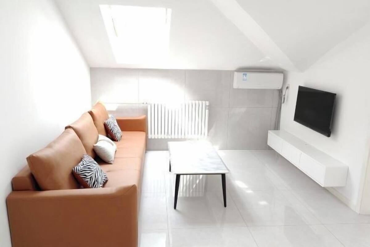 A modern living room with a sofa, a coffee table, a TV mounted on the wall, and a radiator.
