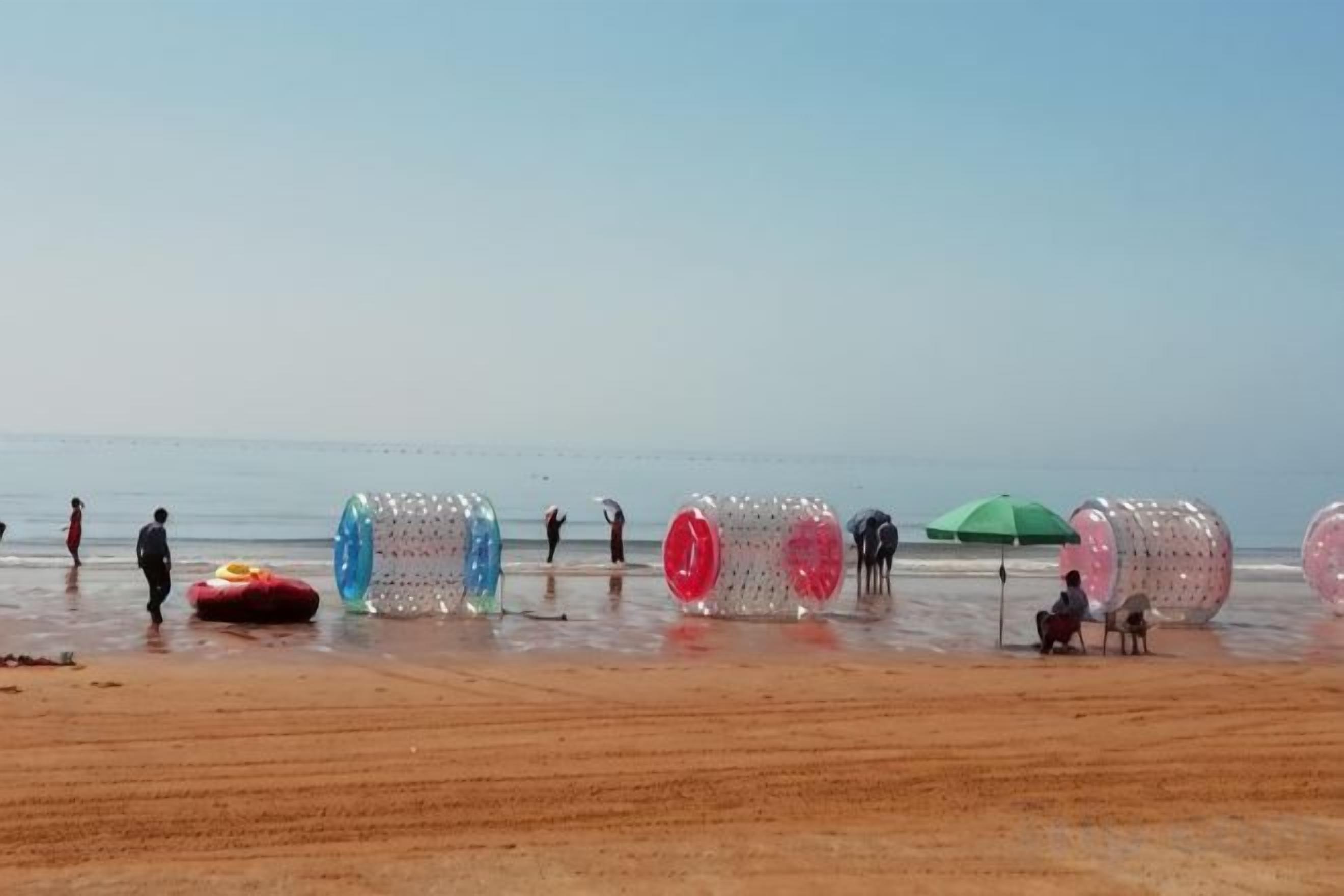 A beach with people, colorful inflatable tubes, and a green umbrella.