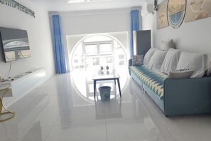A modern living room with a sofa, a TV, a dining table, and a view through a large window. - Qingdao Tianze Seaview Apartment (Qingdao)