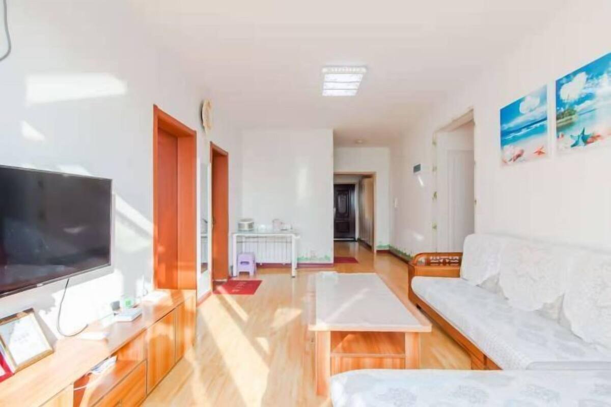 A modern living room with a flat-screen TV, wooden furniture, a white sofa, and a small table.