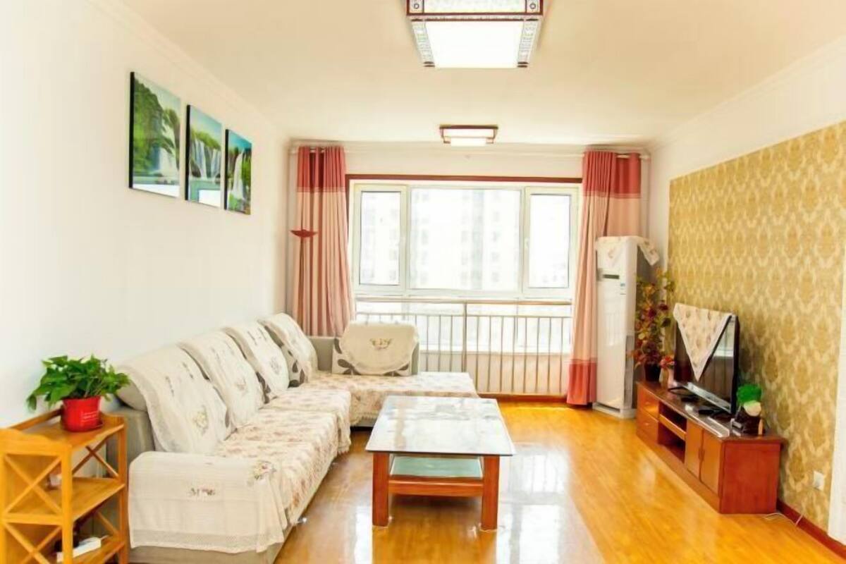A living room with a sofa, a coffee table, a TV stand, and a window with curtains.