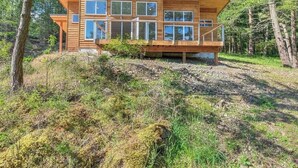 Una cabana de fusta moderna amb diverses finestres, una terrassa i envoltada de bosc.