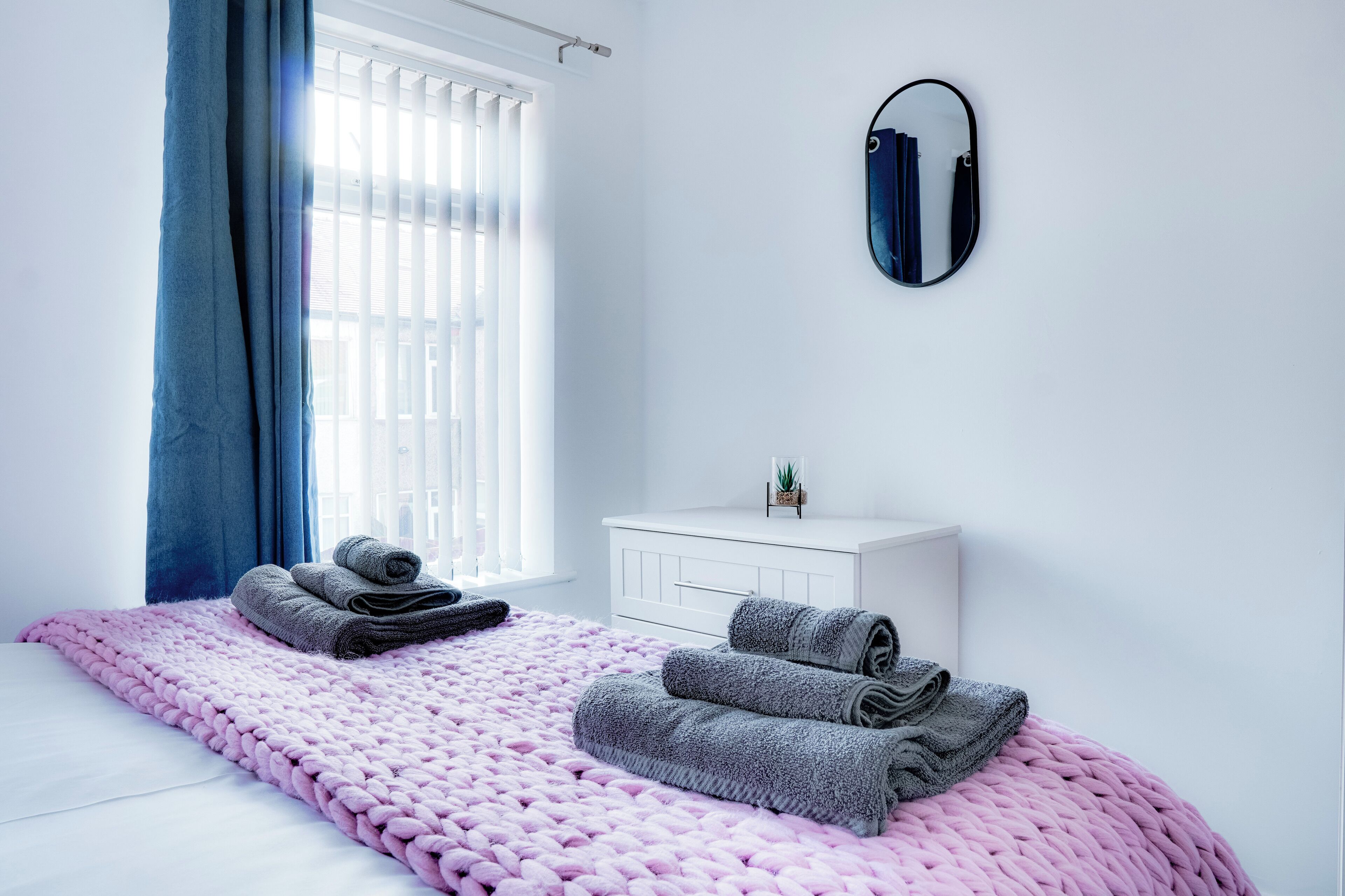 A bedroom with a bed, a white dresser, a mirror, and a window with curtains.