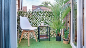 Un petit espace patio avec une chaise blanche, une table en bois et une plante en pot.