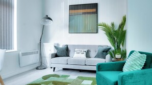 Un salon moderne avec un canapé gris, un fauteuil turquoise et un tapis à motifs verts.