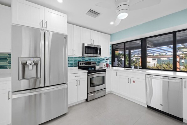 A modern kitchen with stainless steel appliances, white cabinets, and a large window with a view of greenery.