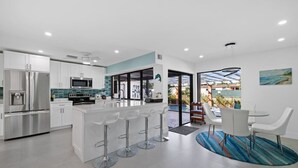 Een moderne keuken met een centraal eiland, roestvrijstalen apparatuur en een eetgedeelte met witte stoelen en een blauw gestreept vloerkleed.