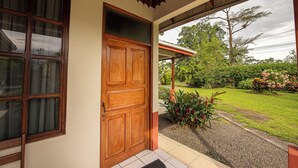 A wooden door with a glass panel and a number "2" on it, leading to a covered porch with a view of a garden and trees. - Befox Adventure (La Fortuna)