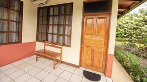 A wooden bench outside a building with a tiled floor and a door. - Befox Adventure (La Fortuna)