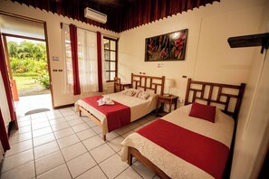 A hotel room with two beds, a window with curtains, a painting on the wall, and an air conditioning unit. - Befox Adventure (La Fortuna)