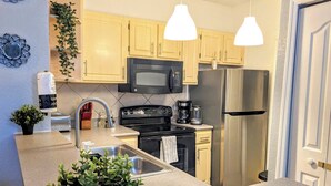 Una cucina moderna con mobili in legno chiaro, elettrodomestici in acciaio inossidabile, un piano di lavoro in granito e luci a sospensione.