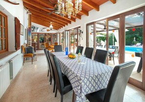 A dining area with a table set for six, a ceiling fan, and a view of a swimming pool outside. - Charming Country House, A/C, Private Pool, Extensive Grounds, Superb Views - 5mins drive to Pollenca (Pollença)