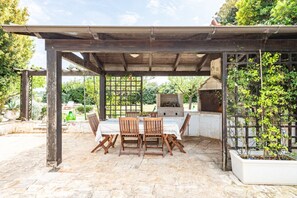 An outdoor patio with a pergola, a grill, and a table with chairs.