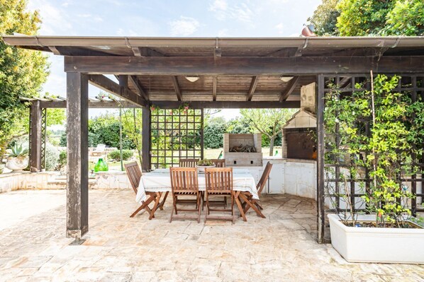 An outdoor patio with a pergola, a grill, and a table with chairs.