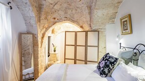 Ein Schlafzimmer mit einem steinernen Bogen, einem Bett mit weißer Bettwäsche, einem hölzernen Kleiderschrank und einem Nachttisch mit einer Lampe.