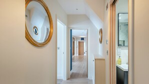 A hallway with a wooden floor, white walls, and a mirror on the left. There is a door at the end of the hallway leading to another room. - Station Street Apartment (Cockermouth)