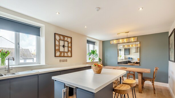 A modern kitchen with a central island, dark cabinetry, and a large window. - Station Street Apartment (Cockermouth)