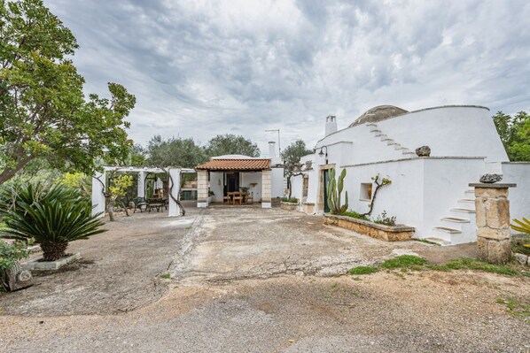 A white building with a tiled roof, a stone staircase, and a garden area with a bench and plants.