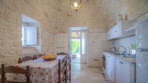 A stone-walled room with a dining table, chairs, a kitchen with cabinets, and a window. - Trullo Corbezzolo by Rentbeat (Locorotondo)
