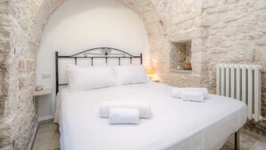 A bed with white linens and towels, a stone wall, and a white radiator. - Trullo Corbezzolo by Rentbeat (Locorotondo)