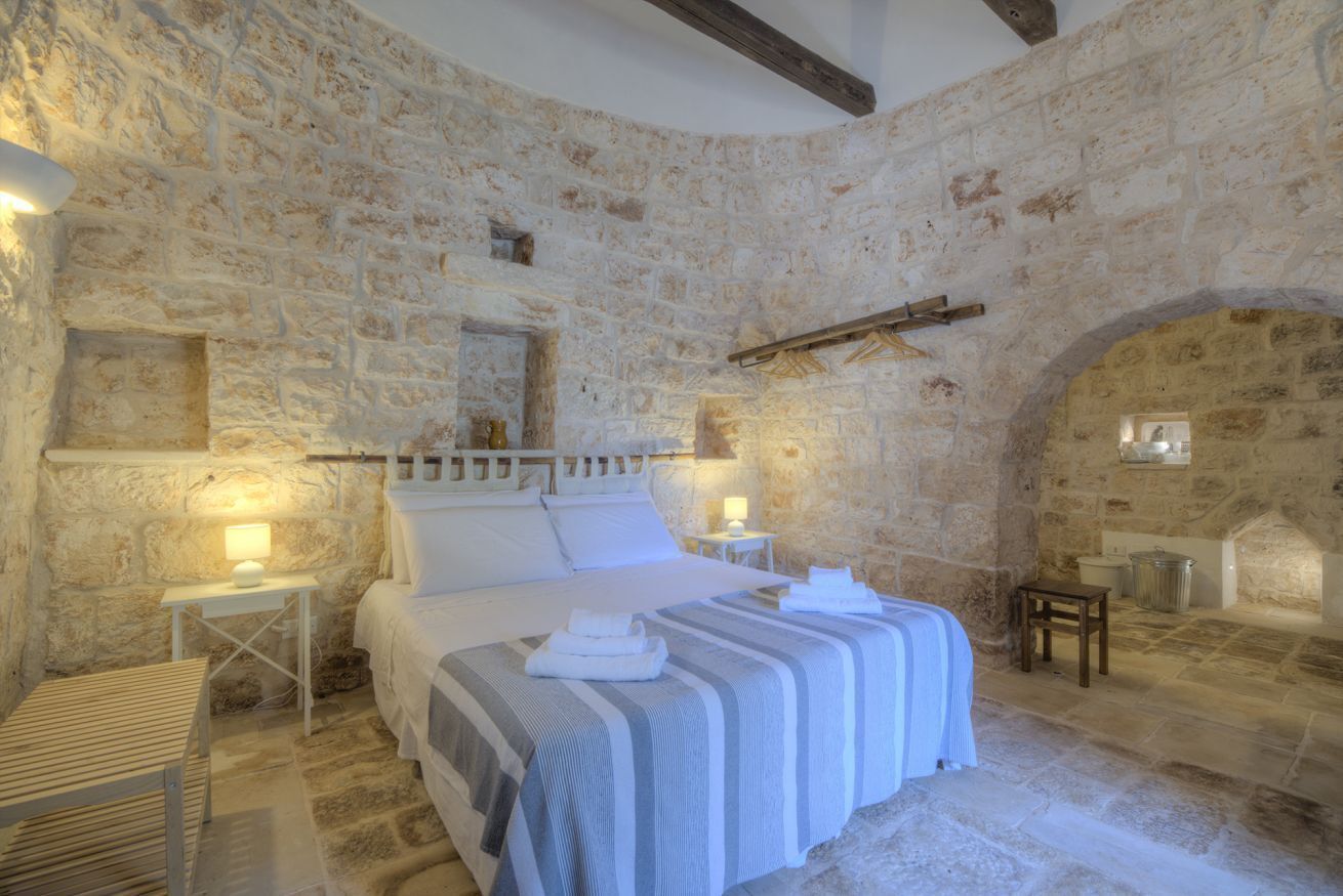 A stone-walled bedroom with a bed, bedside tables, and a small wooden stool.