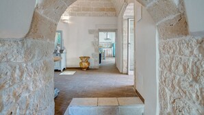 A stone archway leading to a hallway with a tiled floor, a bench, and a vase on a table. - Villa Philos by Rentbeat (Sorbola)