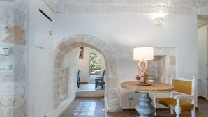 A stone-walled room with a round table and a chair, a doorway leading to another room, and a light fixture on the wall. - Villa Philos by Rentbeat (Sorbola)