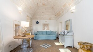 A room with a stone ceiling, a round table with a lamp, a blue sofa, a cabinet with decorative items, and a large vase. - Villa Philos by Rentbeat (Sorbola)