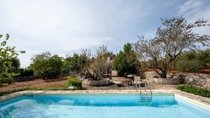 En swimmingpool med stige, omgivet af træer og en stenvæg.