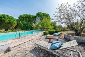 A poolside area with a stone deck, lounge chairs, and a wooden table.