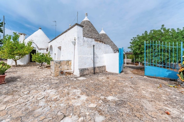 A white building with a tiled roof, a stone wall, and a blue gate.