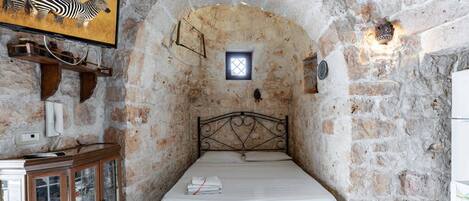 Una habitación de paredes de piedra con una cama, un ventanal pequeño, un armario de madera y un cuadro de cebra en la pared.
