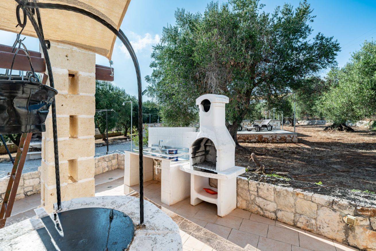 Un área de cocina al aire libre con horno de piedra, un colgador para ollas y una mesa con pileta.
