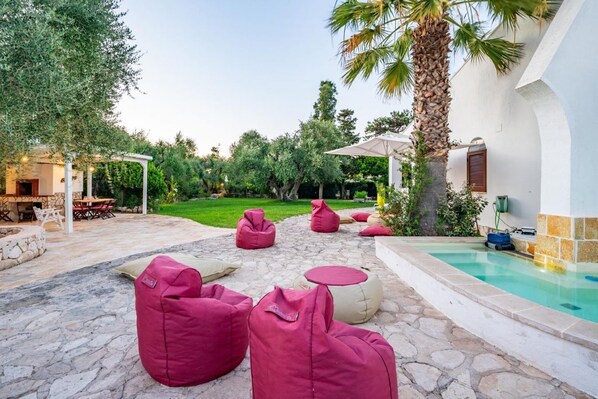 A poolside area with stone flooring, red bean bags, and a covered seating area.