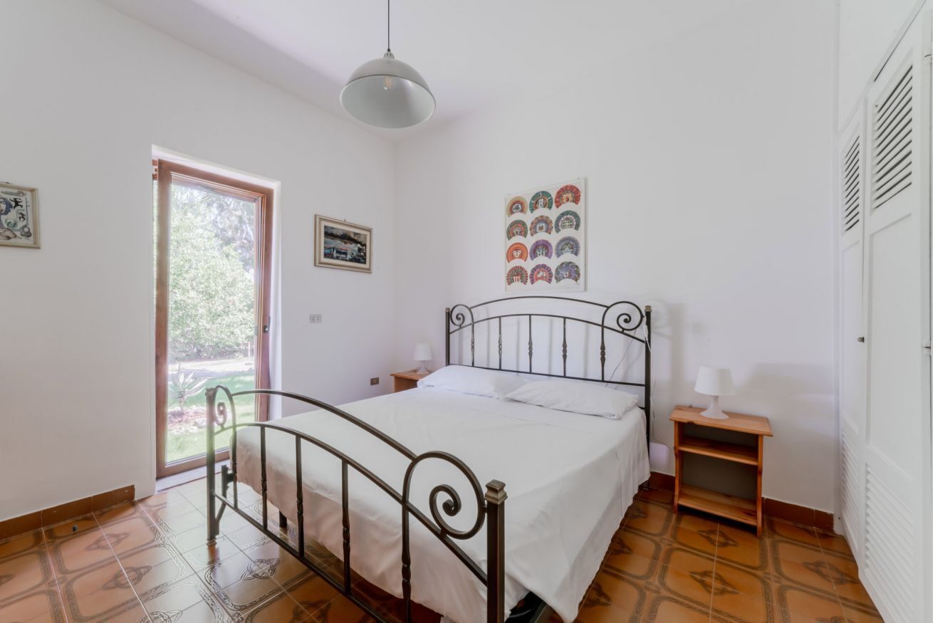 Une chambre à coucher avec un lit, une fenêtre, une porte, une lampe fixée au mur et une petite table.
