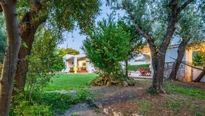 Un jardín con un edificio blanco, un árbol y un muro de piedra.