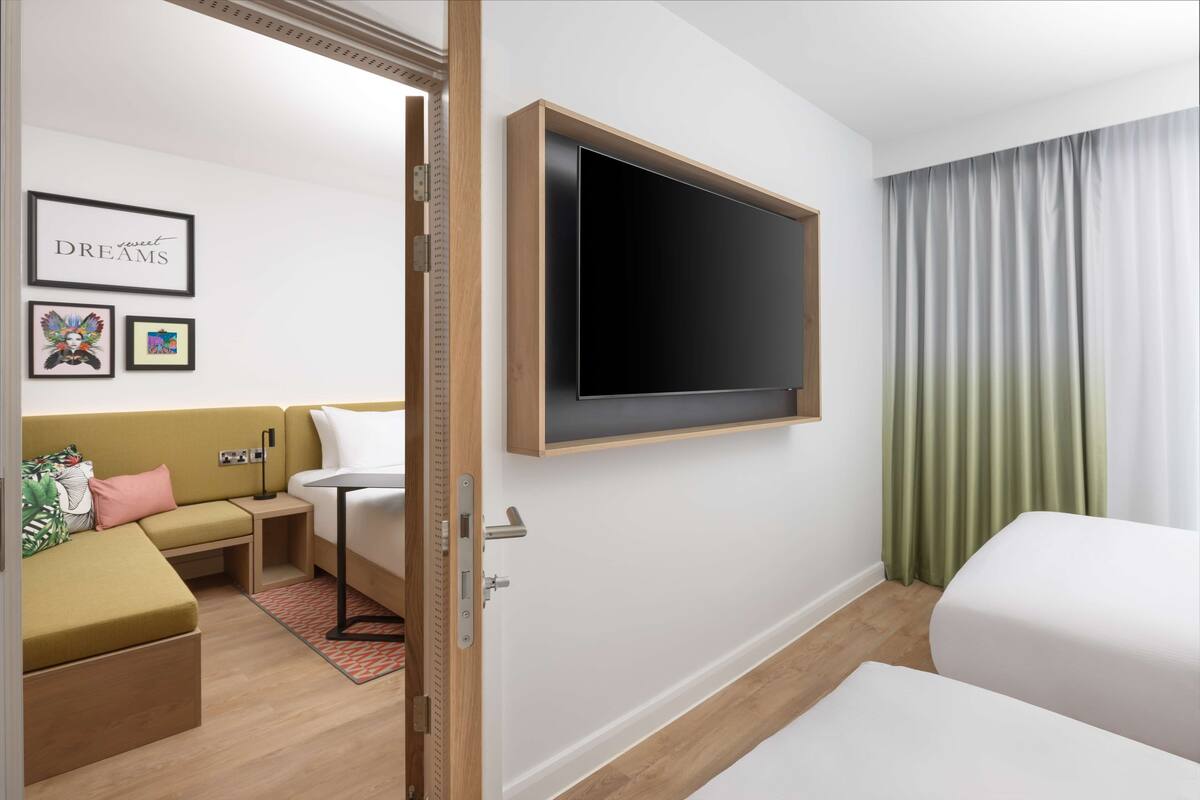 A modern hotel room with a large flat-screen TV mounted on the wall, a sofa, a bed, and a small table.