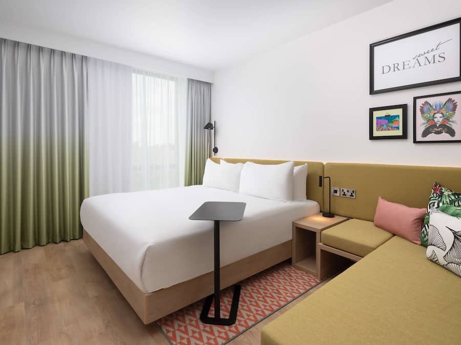 Ein Hotelzimmer mit Bett, Nachttisch, einer Couch, einer Lampe und gerahmten Bildern an der Wand.