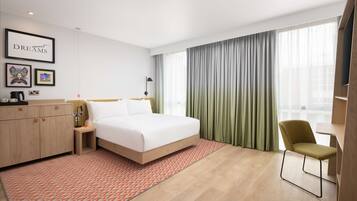 A modern hotel room with a bed, a desk, a chair, a wardrobe, and a large window with curtains.