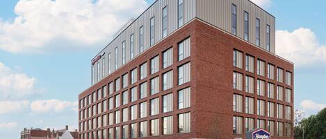 A modern hotel with a brick facade, large windows, and a prominent Hampton sign.