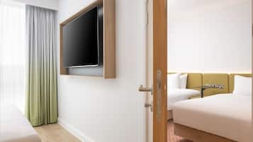 Habitación de hotel con cama, televisión montada en la pared, una mesita y una ventana con cortinas.